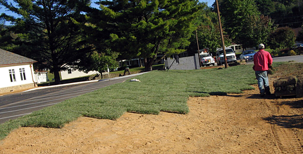 A WNC Landscaping crew member laying rolls of sod on a graded lawn in Waynesville, North Carolina